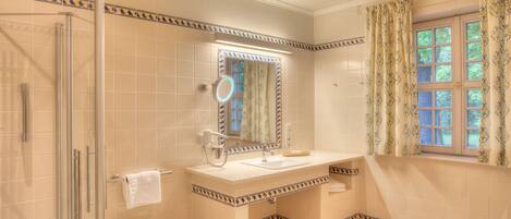 A bathroom with a glass shower enclosure, a sink with a mirror, and a window with curtains.