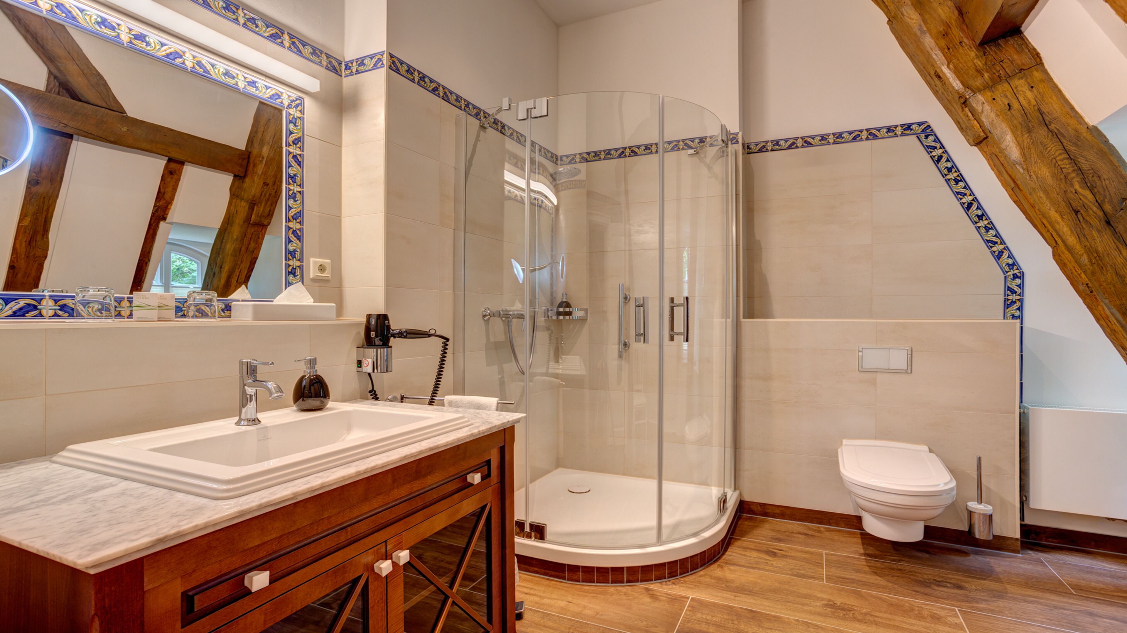 Et moderne badeværelse med en brusekabine med glasdøre, et træbord med marmorplade og et hvidt toilet.