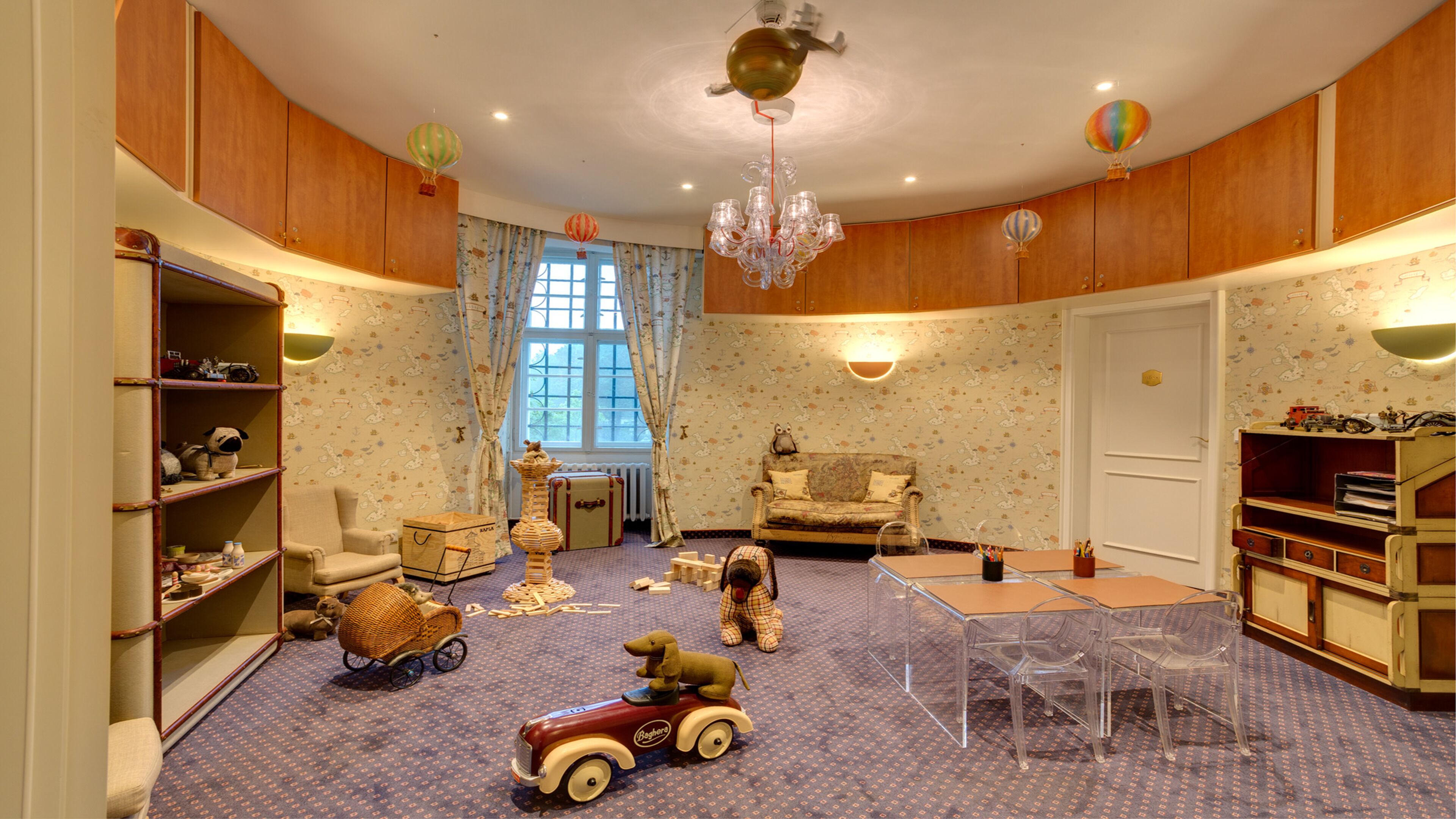 A cozy room with a wooden ceiling, a chandelier, a sofa, a table, and a window with curtains.