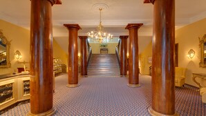 Eine prachtvolle Eingangshalle mit Holzsäulen, einem Chandelier und einem gemusterten Teppich.