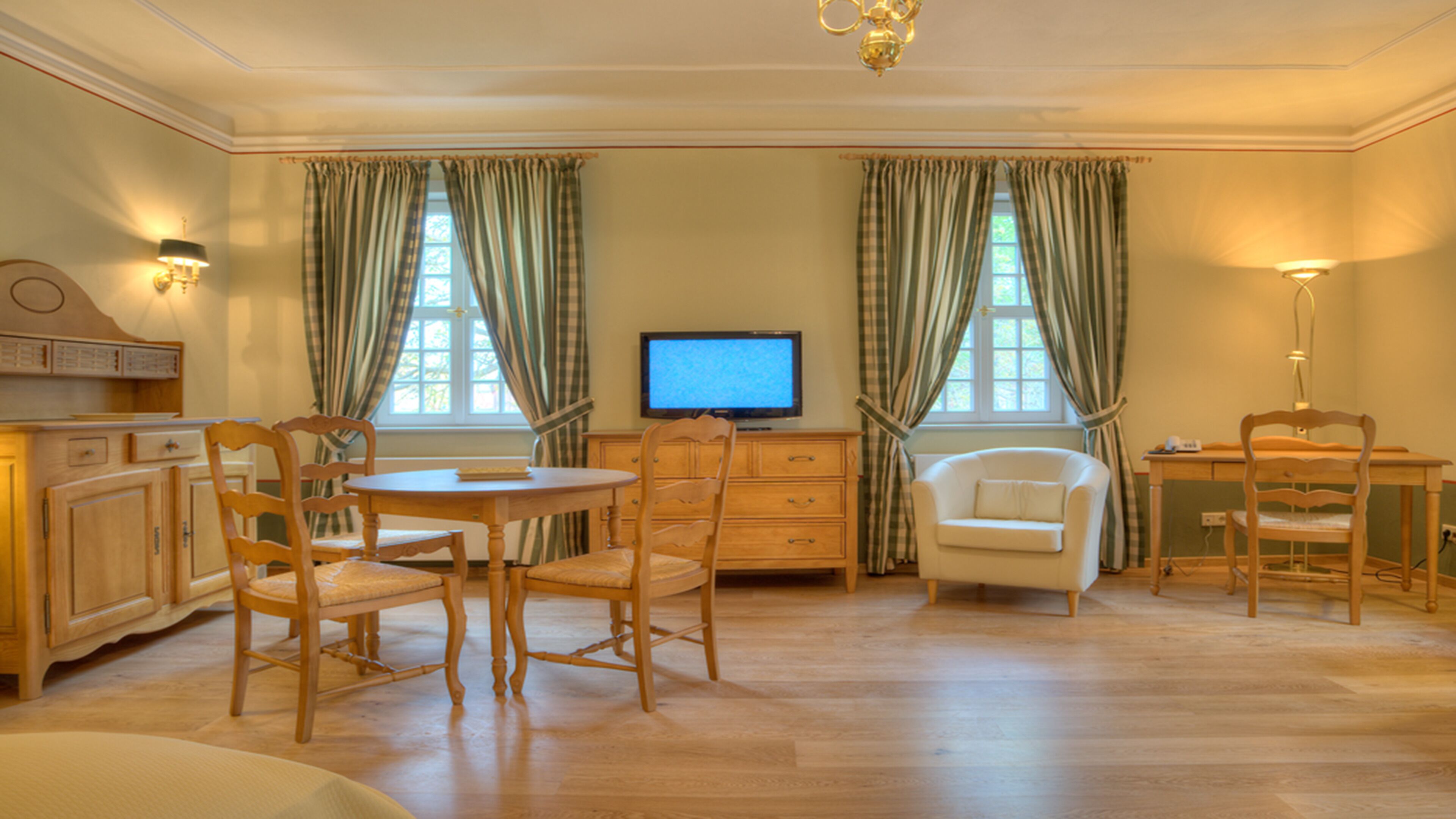 A room with a wooden dining table, two chairs, a television, and a desk with a chair.