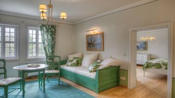 A room with a green sofa, a dining table with chairs, and a painting on the wall.