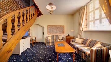 A cozy living room with a wooden staircase, a patterned carpet, a sofa, a coffee table, and a chandelier.