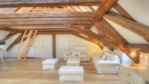Ein Schlafzimmer im Loft-Stil mit freiliegenden Holzbalken, einer weißen Sofagarnitur, einem kleinen Tisch und einer Leiter.