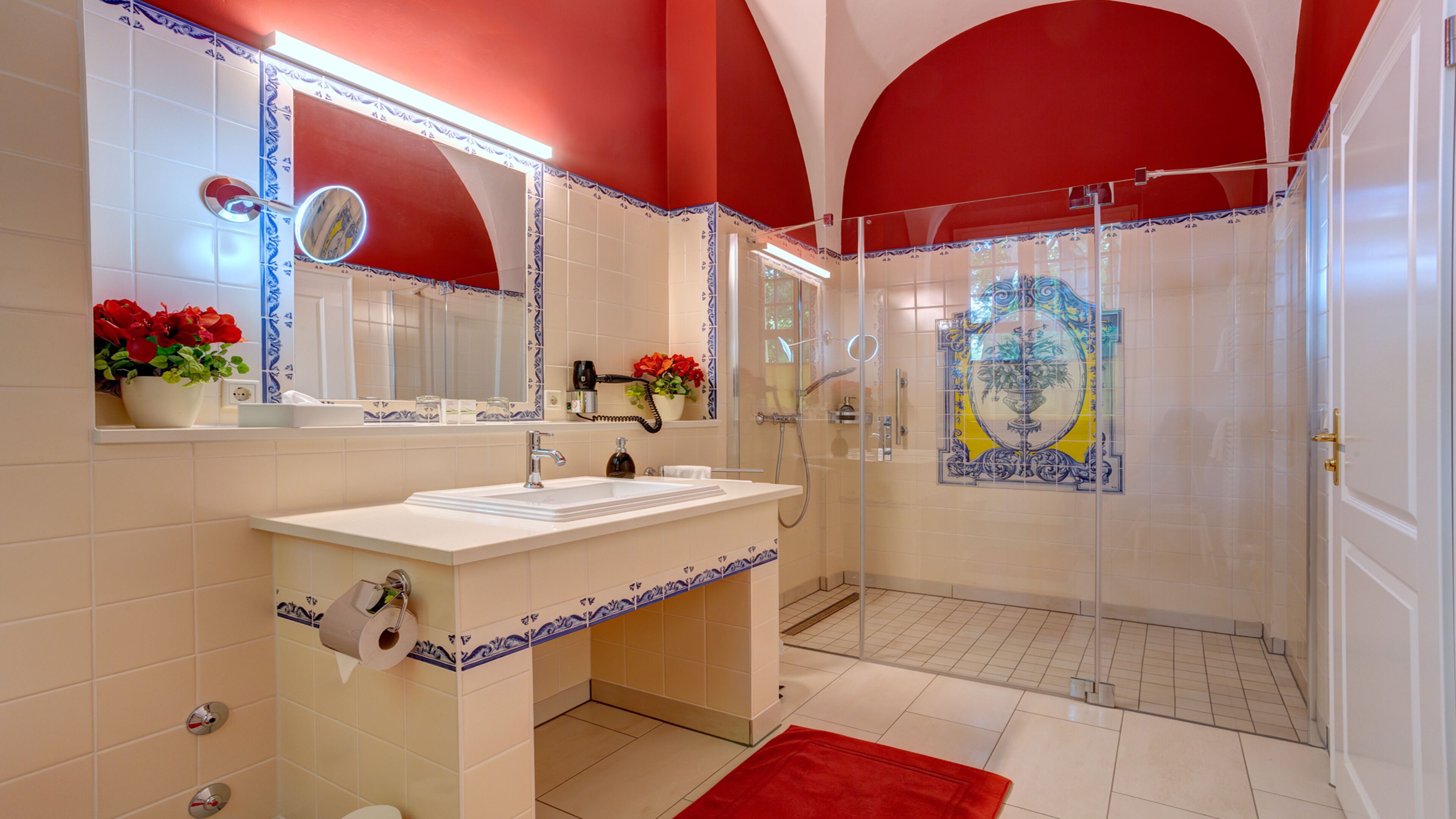 Baño con lavamanos blanco, espejo y paredes rojas.