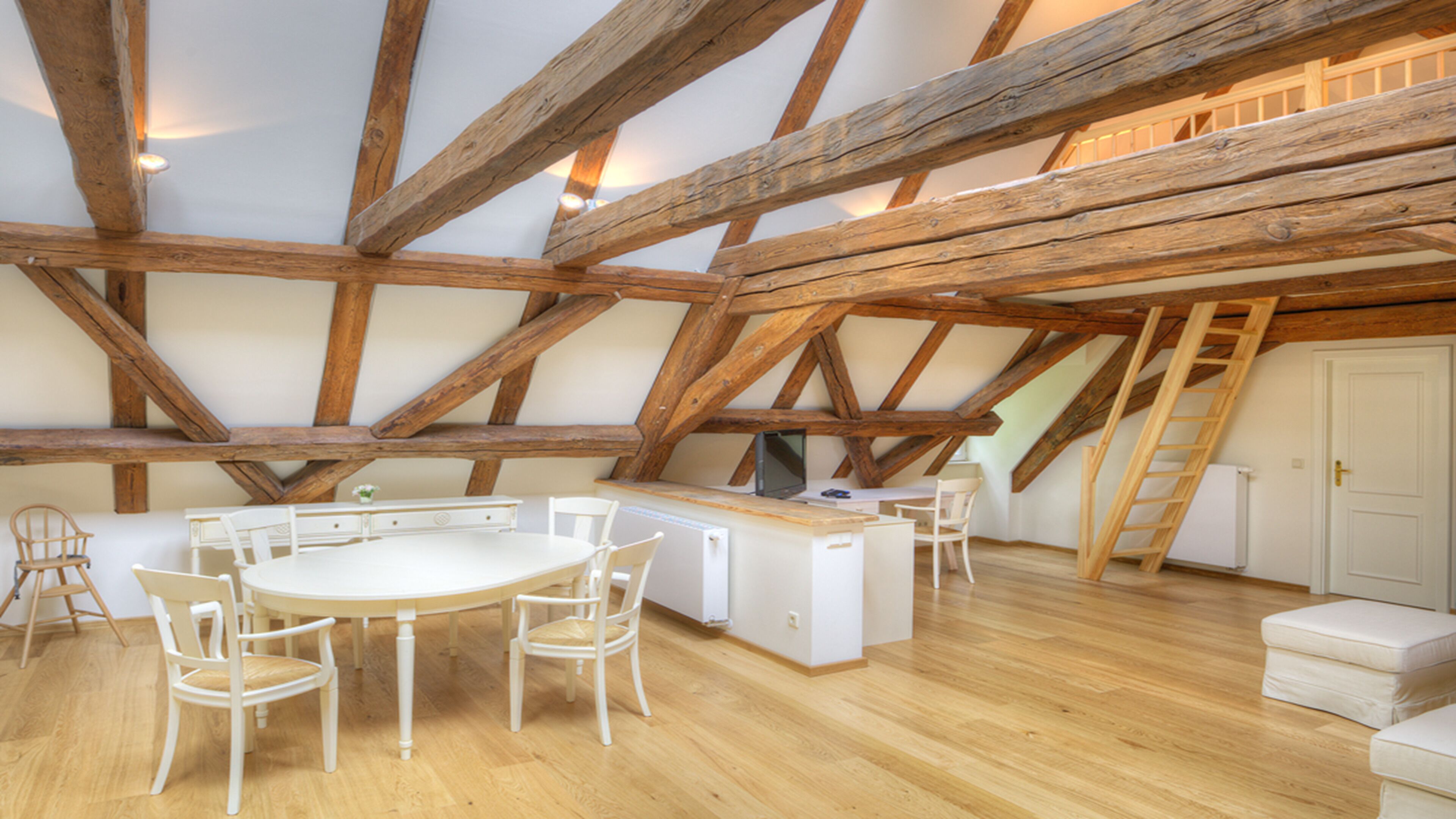 Una habitación con techo de madera, una mesa redonda con sillas, un armario blanco y una puerta blanca.
