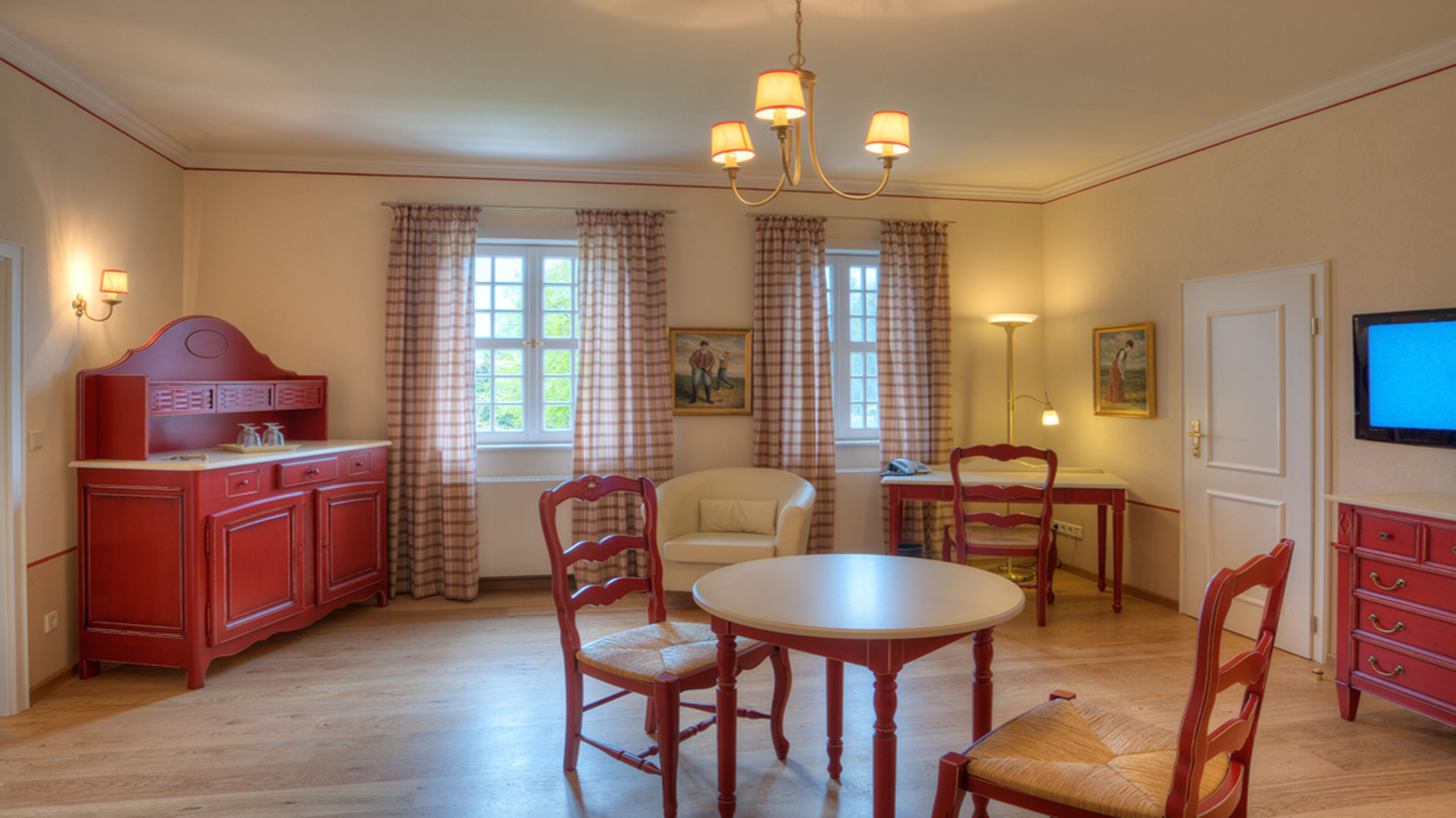 A dining area with a round table, four chairs, a red cabinet, a television, and a painting on the wall.