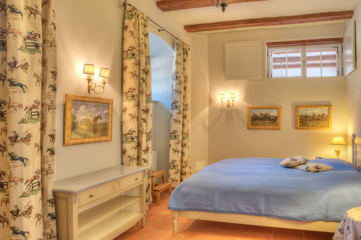 Un dormitorio con cama, mesita de noche, lámpara y ventana.