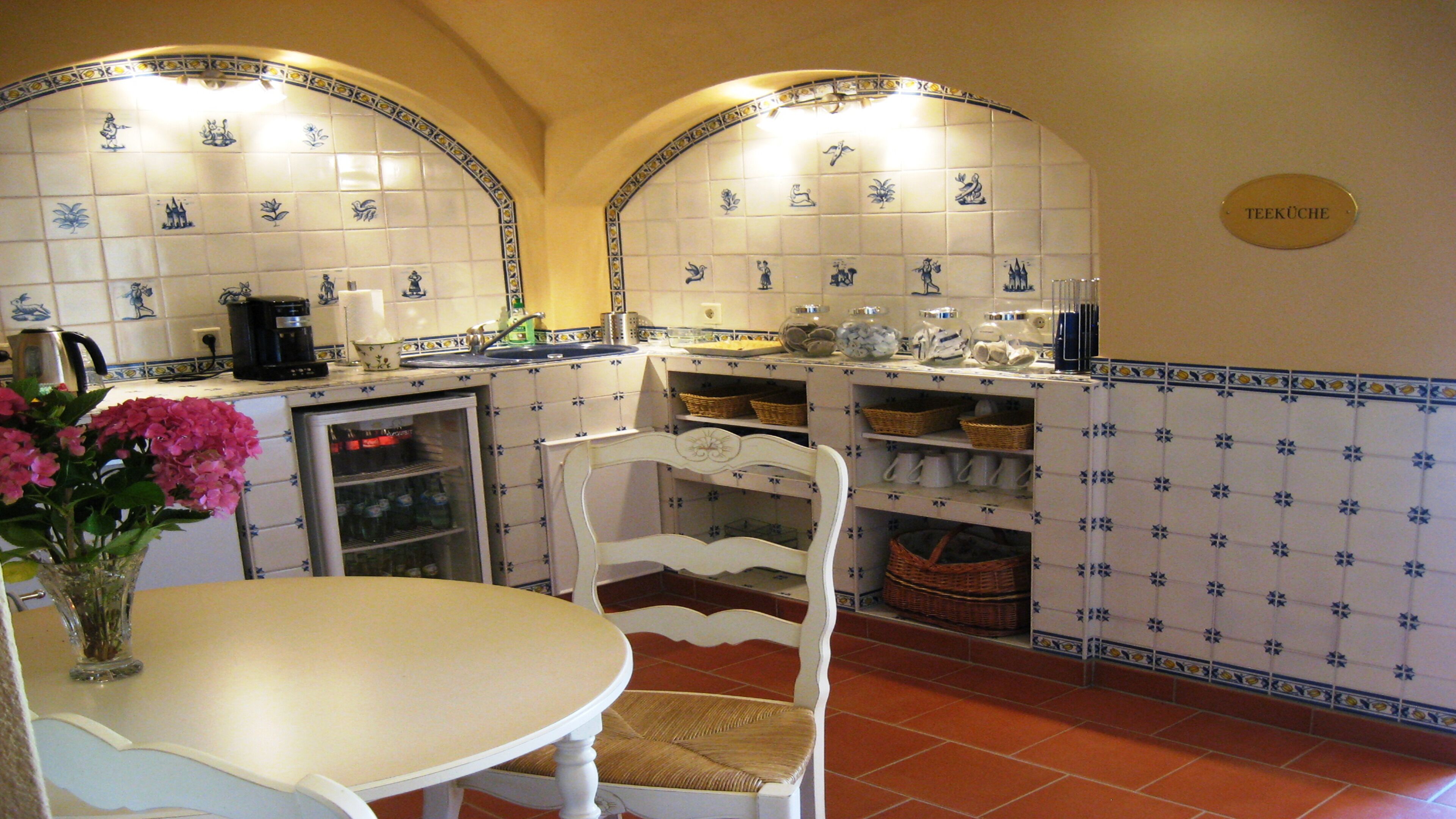 A kitchen with white and blue tiles, a refrigerator, a sink, and a dining table with chairs.