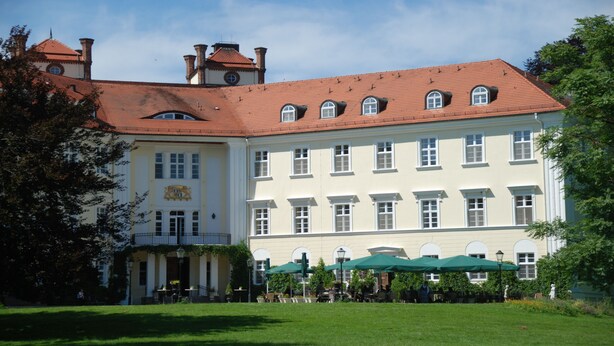 Ein großes, historisches Gebäude mit rotem Ziegeldach, zahlreichen Fenstern und einem zentralen Eingang mit Säulen.