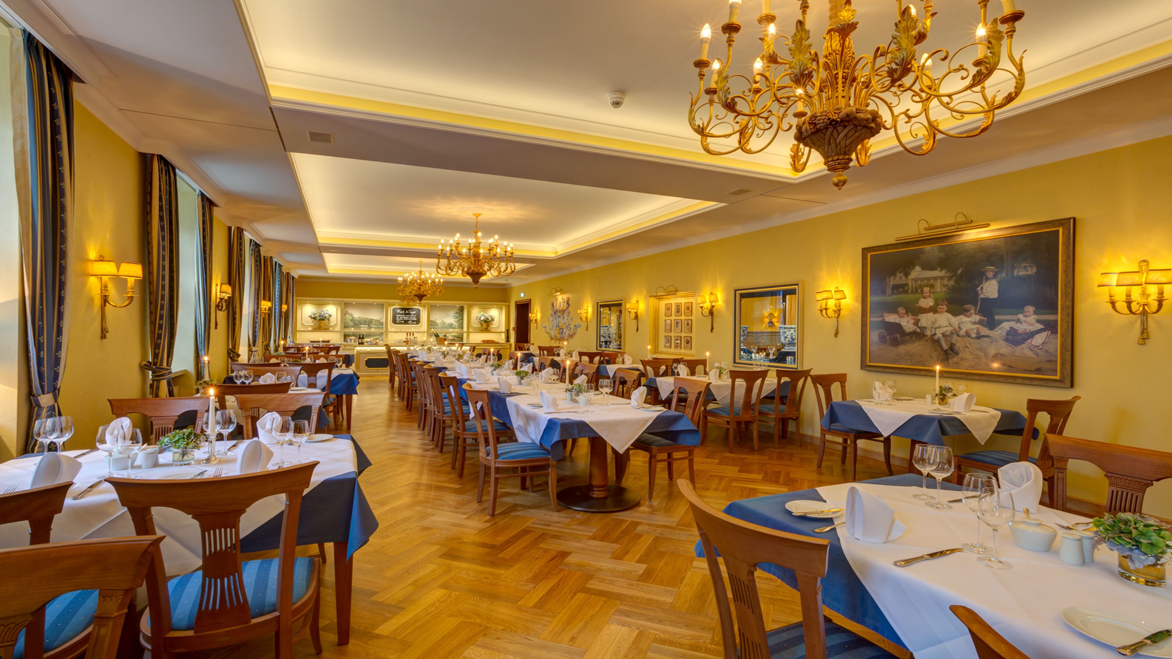 Ein elegantes Esszimmer mit mehreren gedeckten Tischen, Kronleuchtern und Wandleuchten.