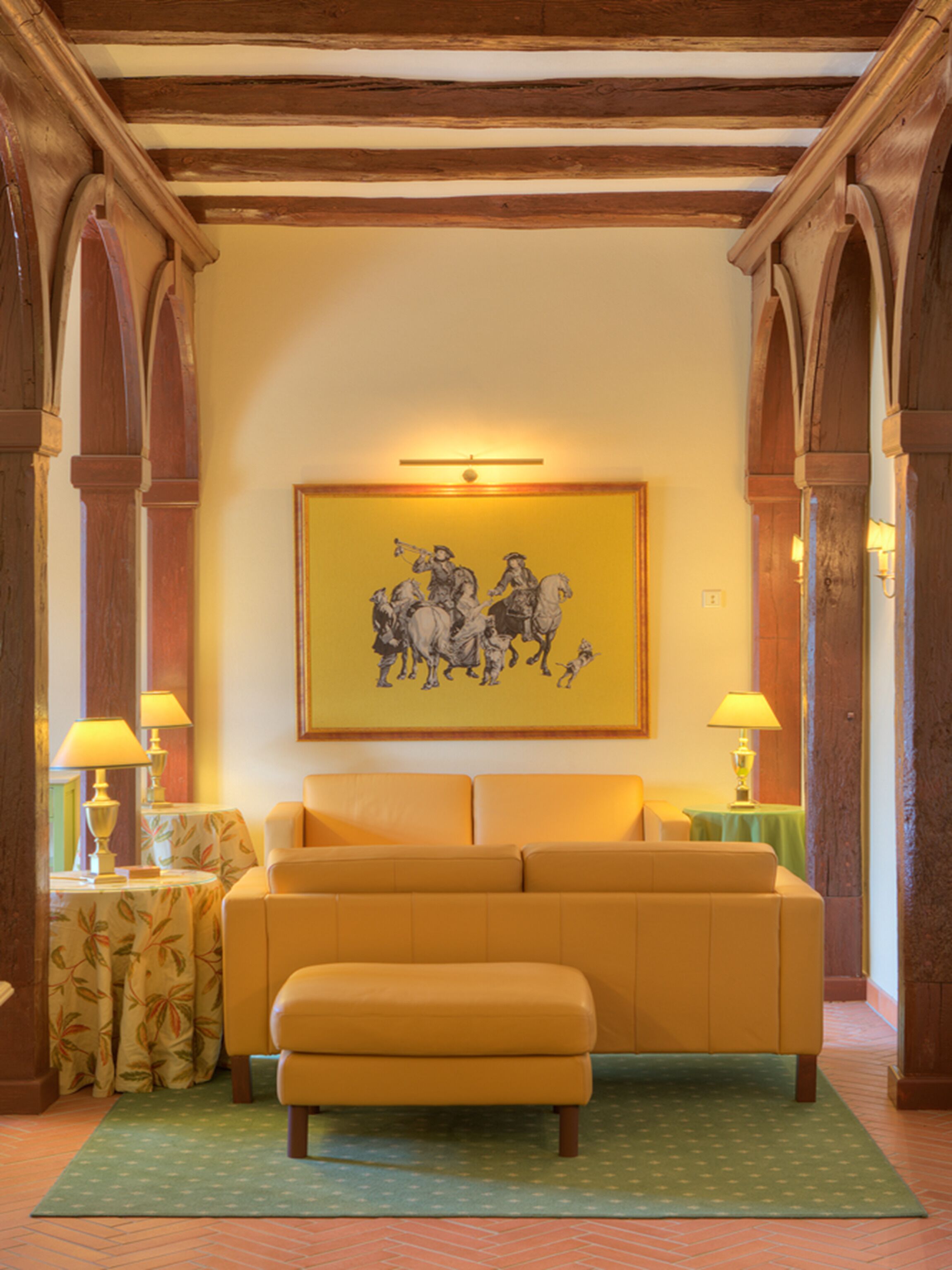 A room with a yellow sofa, a painting of horses, and wooden arches.