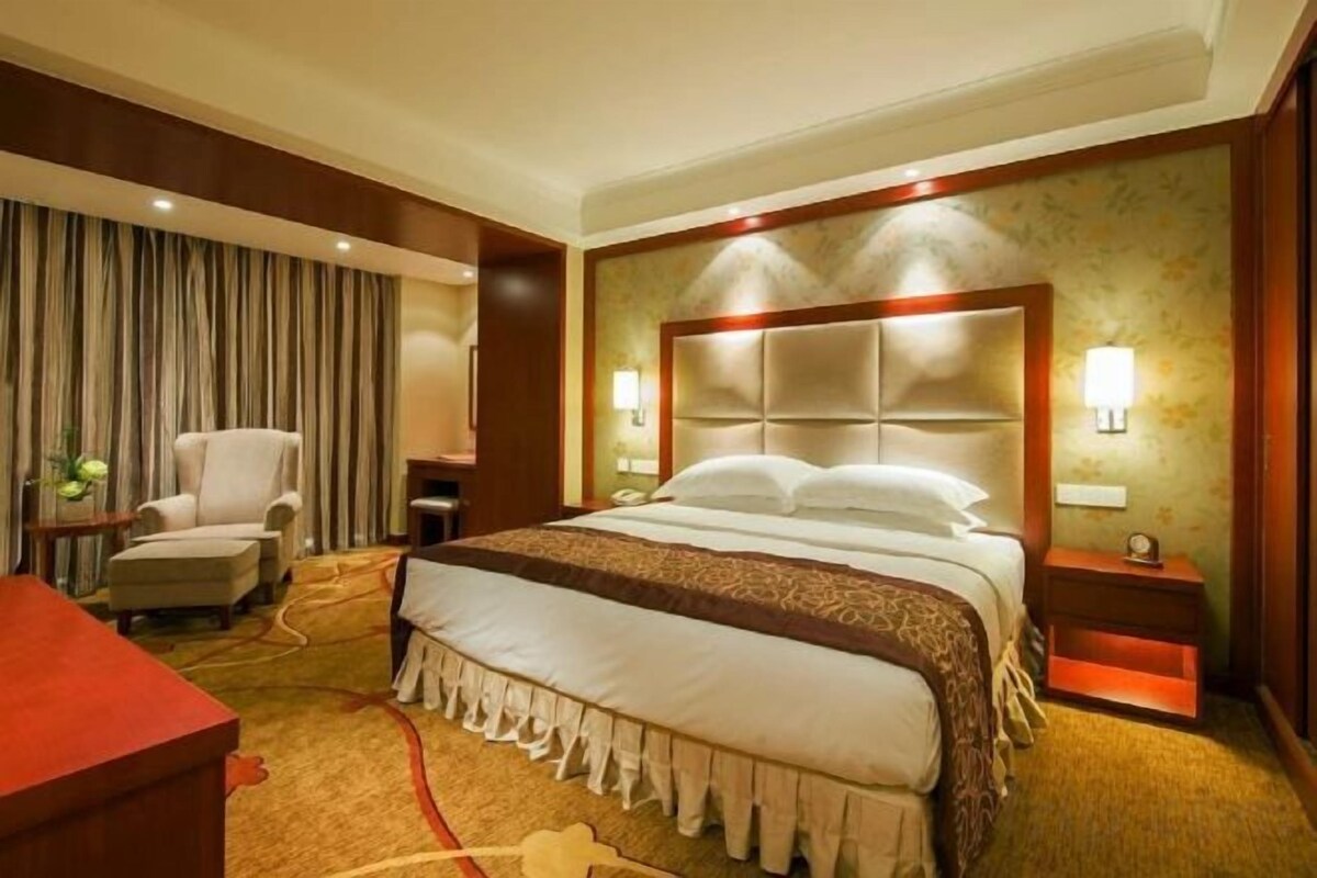 A hotel room with a large bed, a desk, a chair, and a nightstand.