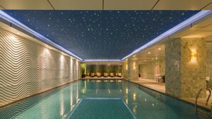 A modern indoor pool with a wavy wall design, a ceiling with a starry night effect, and a seating area with plants.