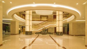 A spacious lobby with a central staircase, marble flooring, and a chandelier.
