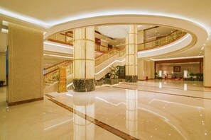 Eine großzügige Lobby mit einer zentralen Treppe, Marmorböden und einer verzierten Decke.