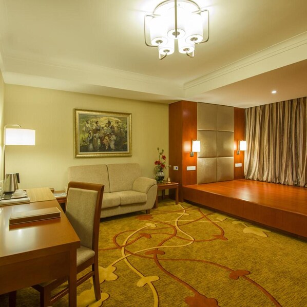 A hotel room with a dining table, a sofa, a painting on the wall, and a carpet with a leaf pattern.