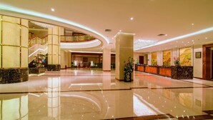 A spacious lobby with a marble floor, a reception desk, and a staircase leading to an upper level.