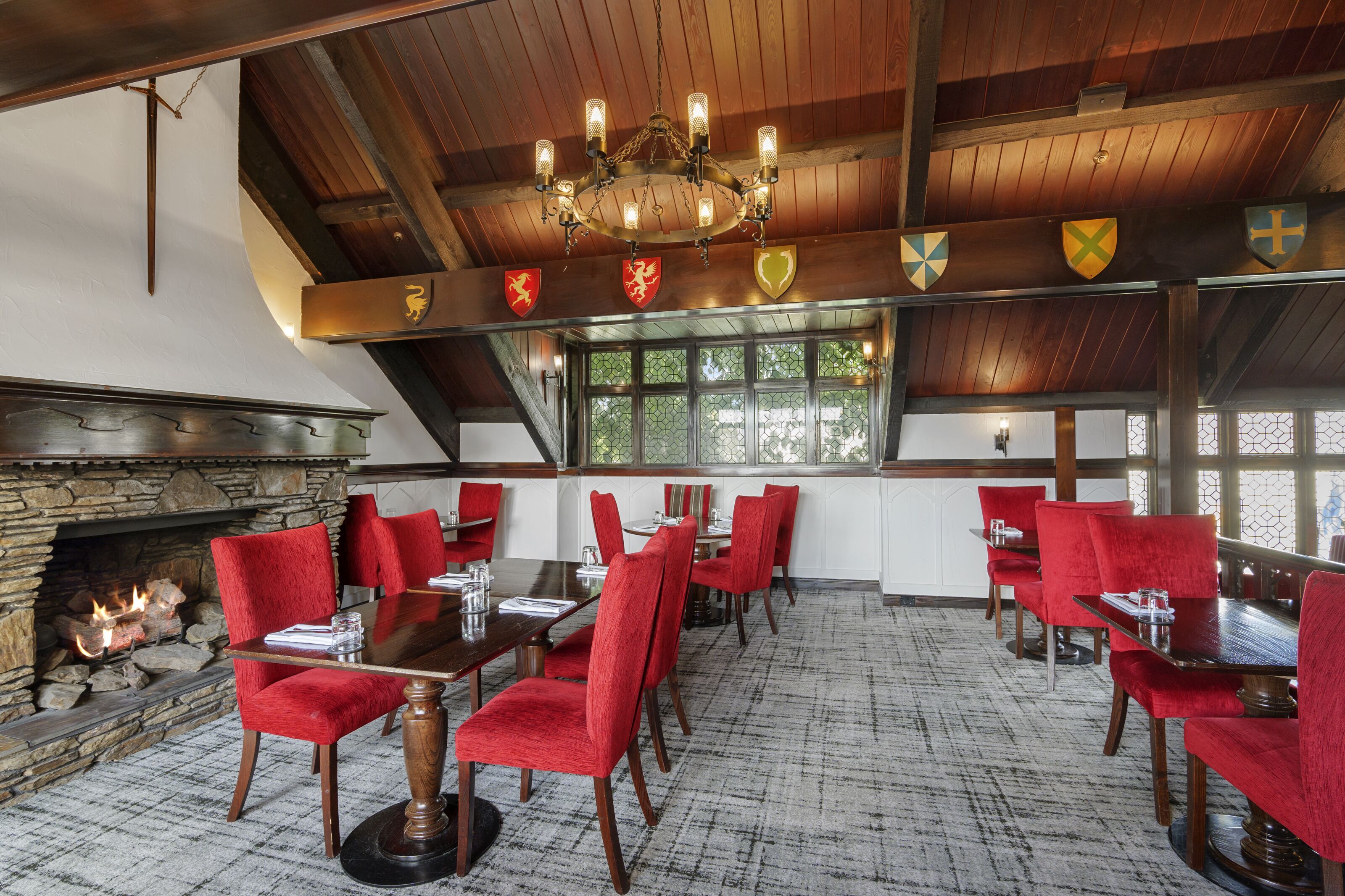 A dining area with red upholstered chairs, a wooden table, a stone fireplace, and a chandelier.