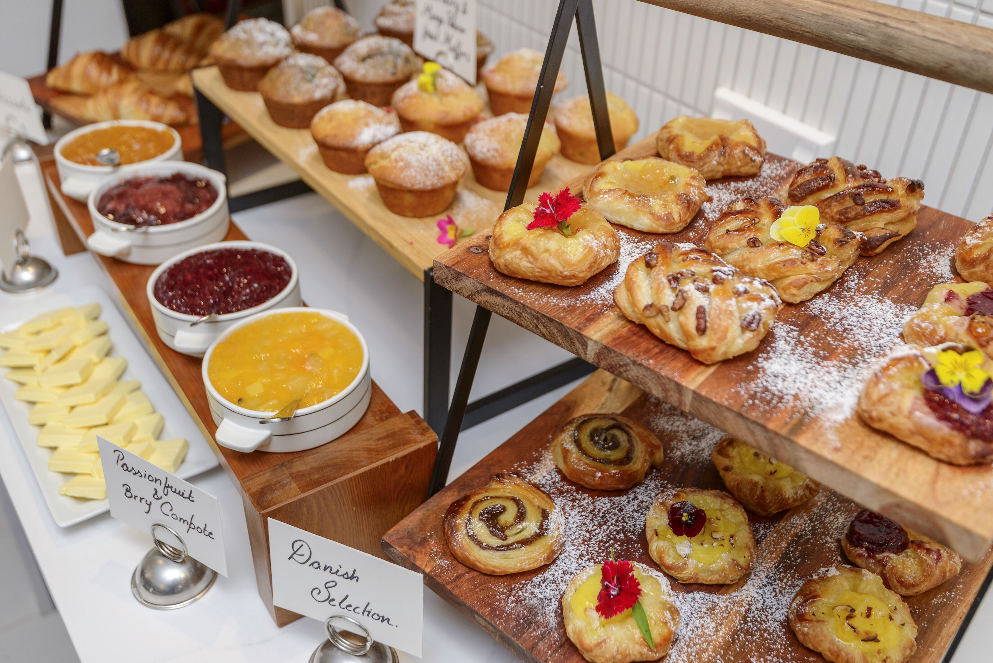 A variety of pastries and desserts on display, including different types of muffins and tarts, with labels indicating flavors like passion fruit and brie compote.
