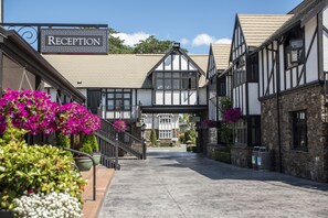 Un espace d’accueil avec un panneau indicateur, un chemin menant à un bâtiment et des compositions florales.