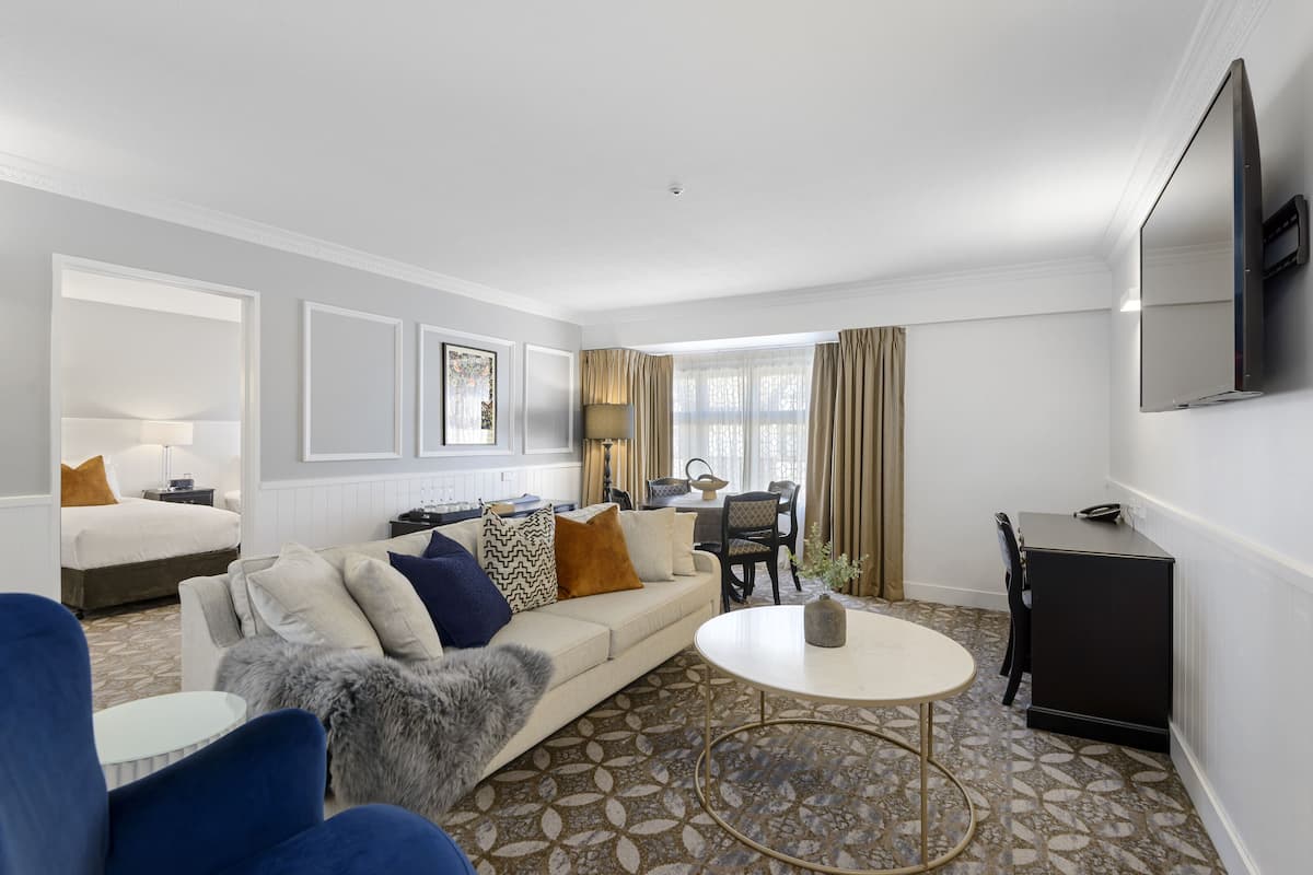 Una habitación de hotel moderna con sofá, sillones, una mesa de comedor y televisor.
