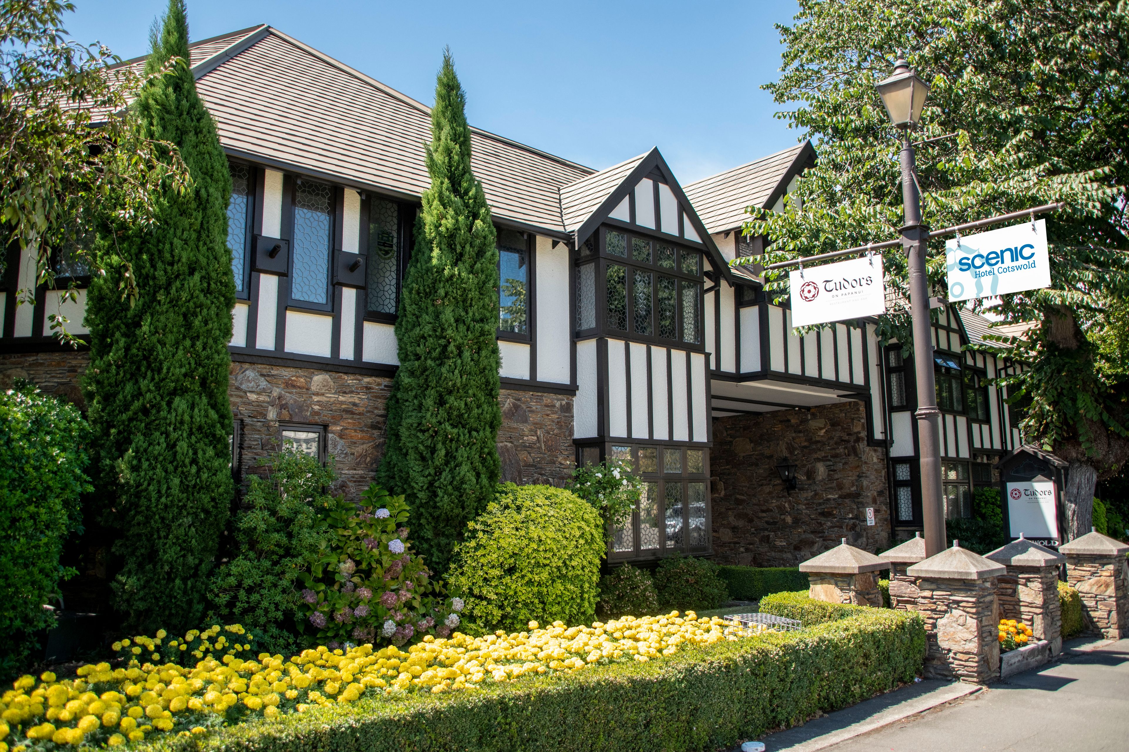 Un edificio de estilo Tudor con fachada de piedra, múltiples ventanas y un letrero que dice 'Tudor's Hotel Cotswold'.