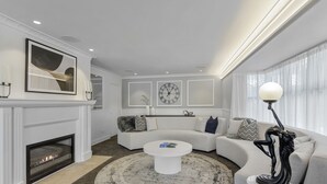 Een moderne woonkamer met een open haard, een ronde salontafel, een zithoek en een grote klok aan de muur.