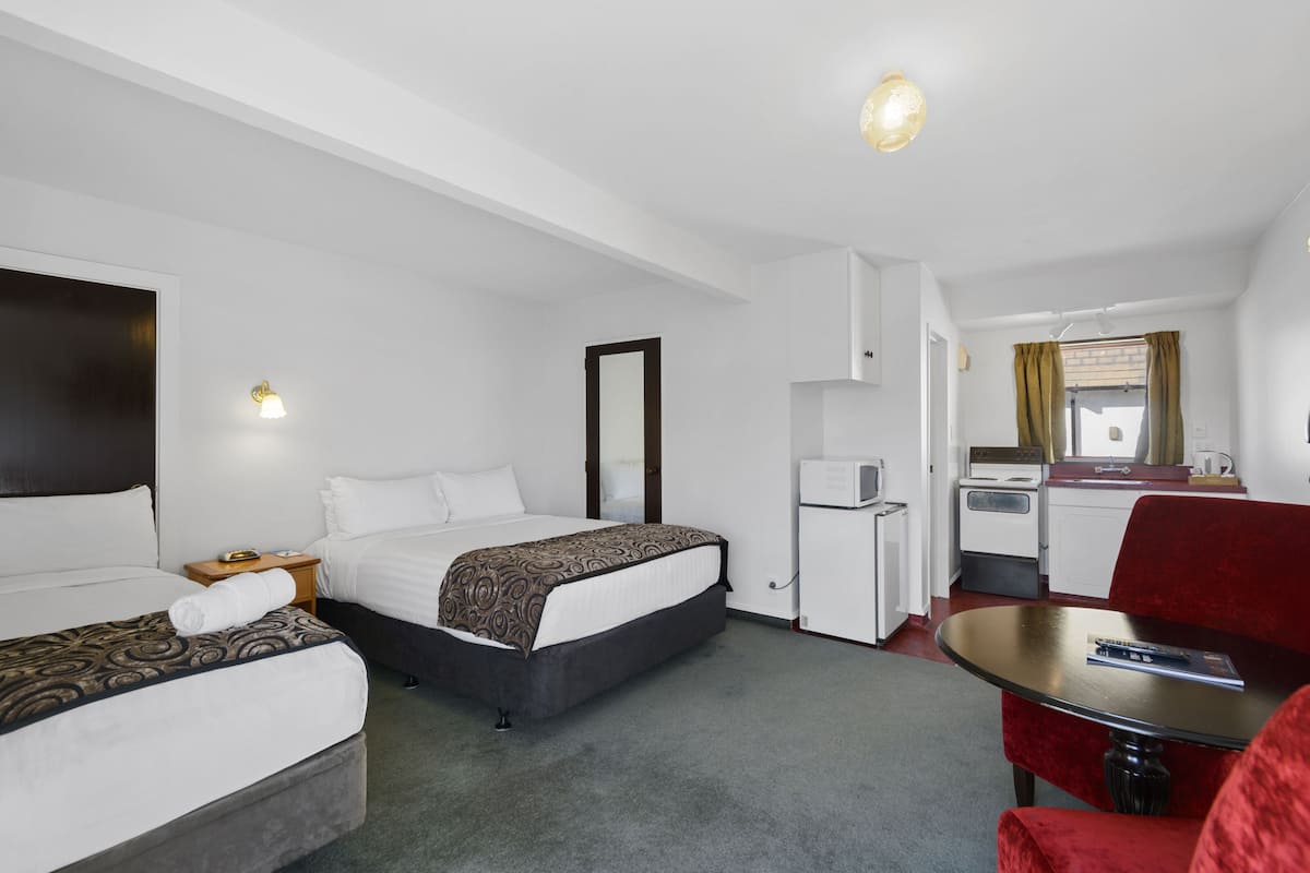 Una habitación de hotel con dos camas, una kitchenette pequeña, una mesa de comedor y una silla roja.