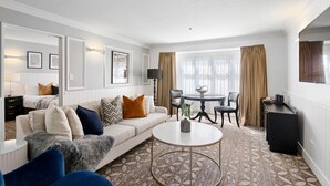 Een moderne hotelkamer met een bank, een rond bijzettafeltje, een eettafel met stoelen en een aan de muur bevestigde televisie.