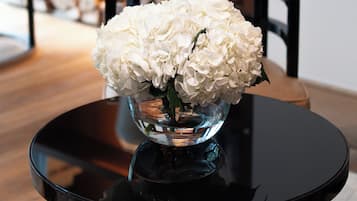 Een eettafel met een glazen vaas gevuld met witte bloemen, een zwarte tafelvoet en een kamerbreed tapijt met een patroon.