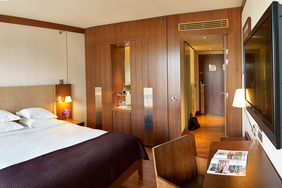 A hotel room with a bed, bedside table, lamp, and a TV.