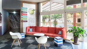 A modern lobby with a red sofa, white chairs, a small table, and a large window with a view of the street. - ibis Sao Jose dos Campos Dutra (São José dos Campos)