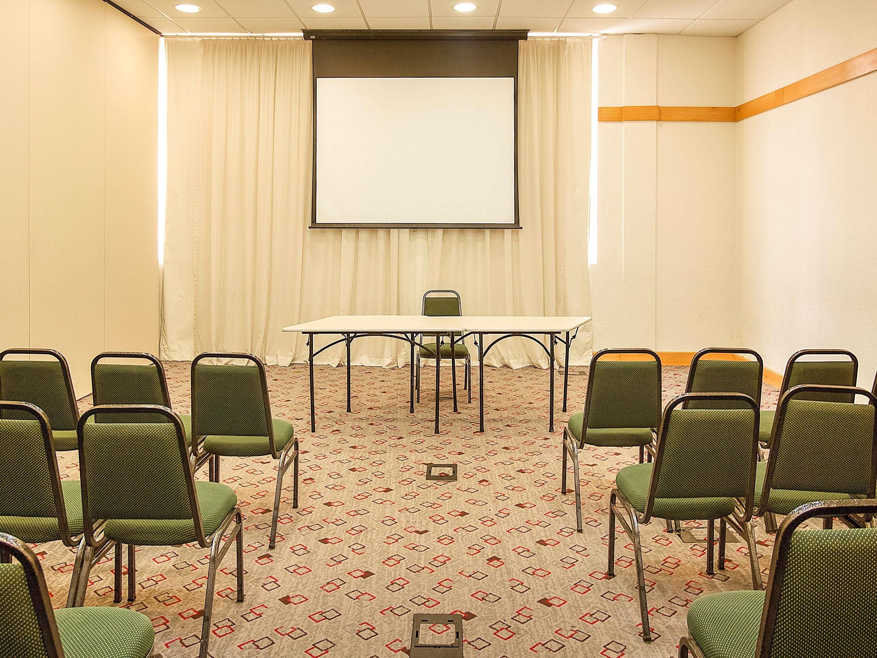 A conference room with a large table, chairs, a projector screen, and a carpeted floor.