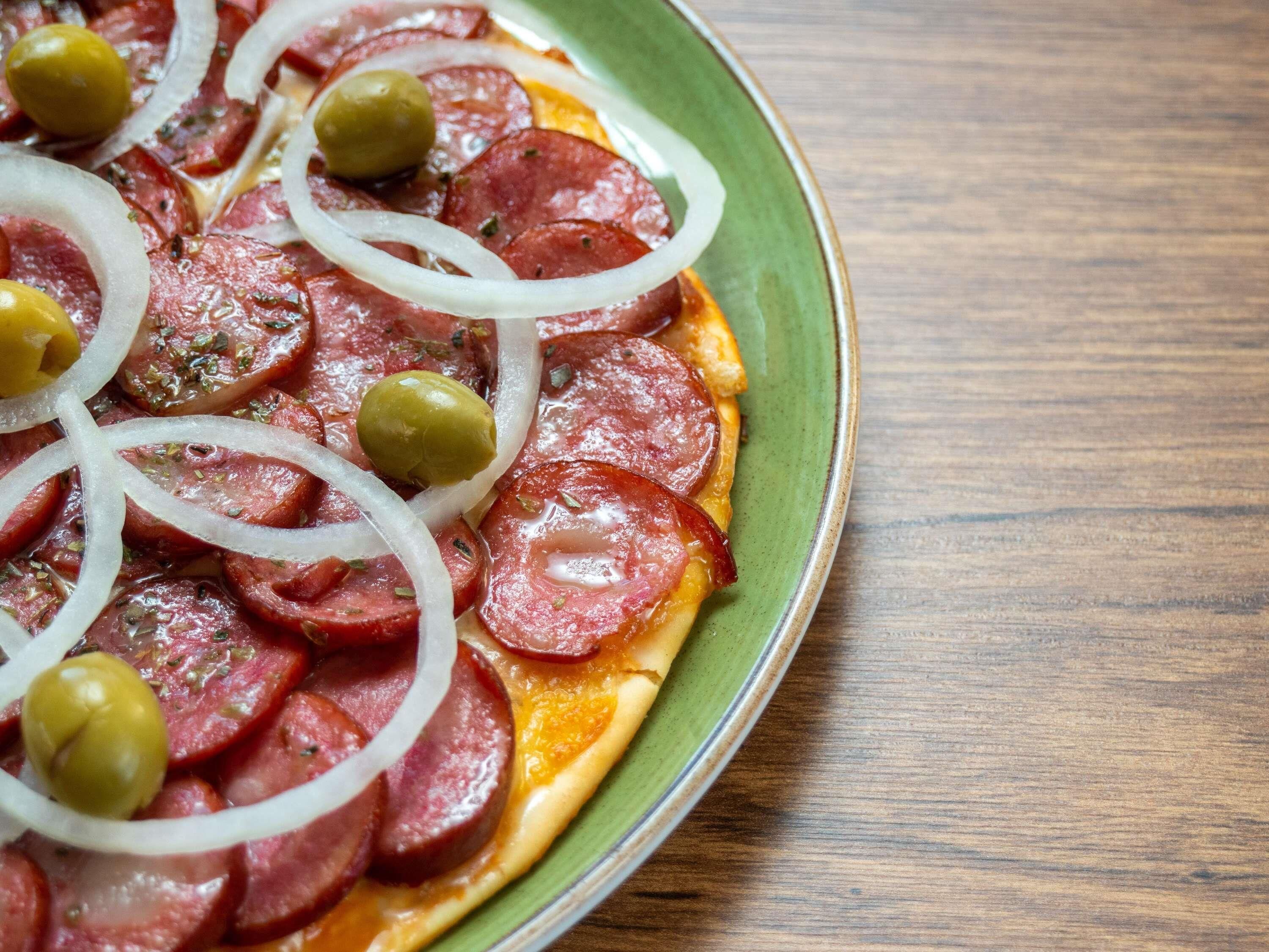 A pizza with pepperoni, onions, and olives on a green plate.