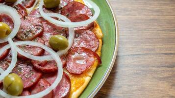 A pizza with pepperoni, onions, and olives on a green plate.