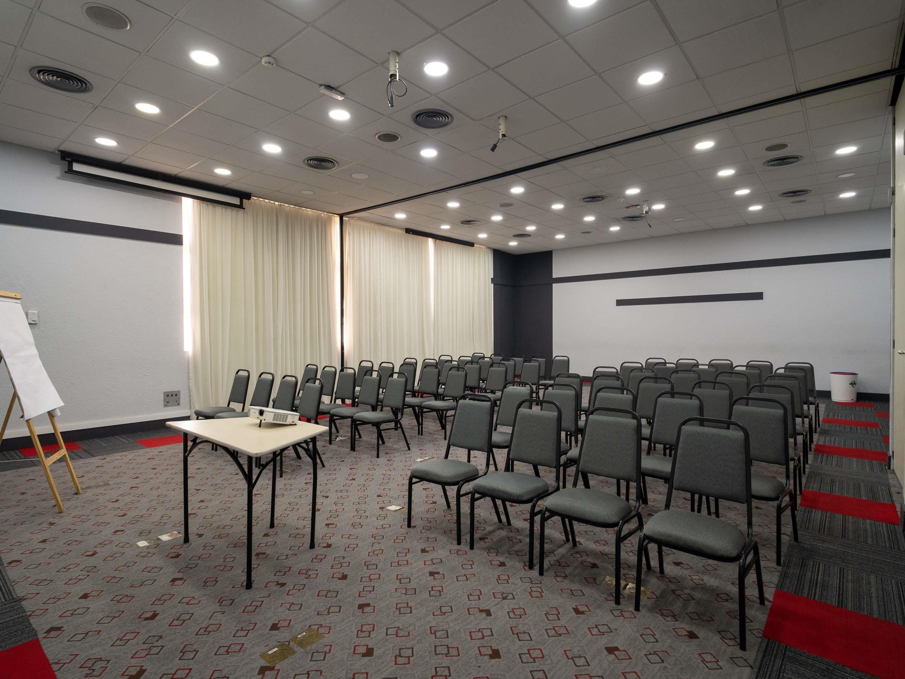 Un salón de conferencias con filas de sillas, un proyector y una pizarra.