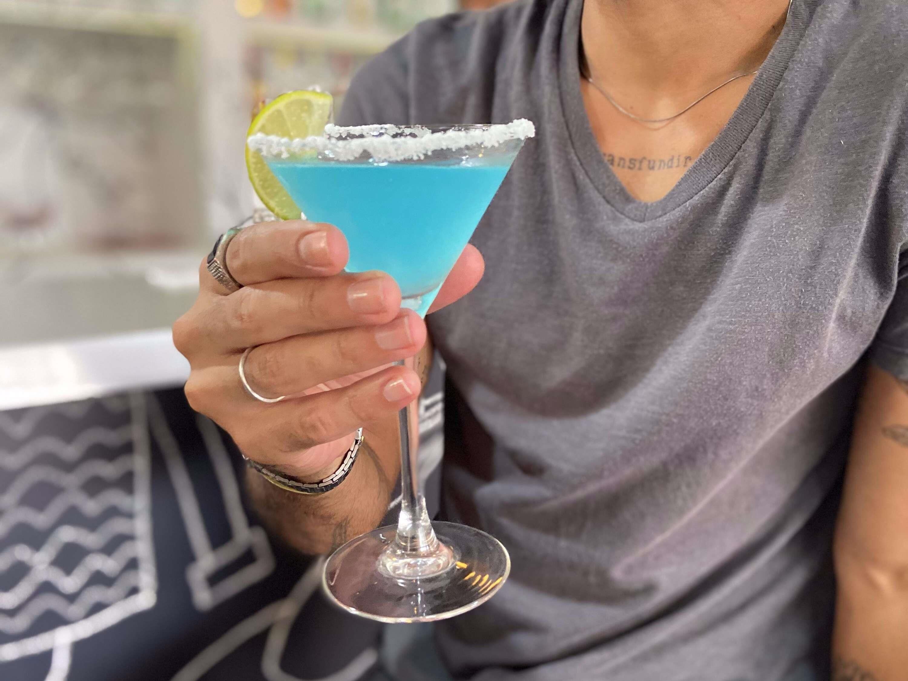 Eine Person hält einen blauen Cocktail mit Limettenspalte und Salzrand.