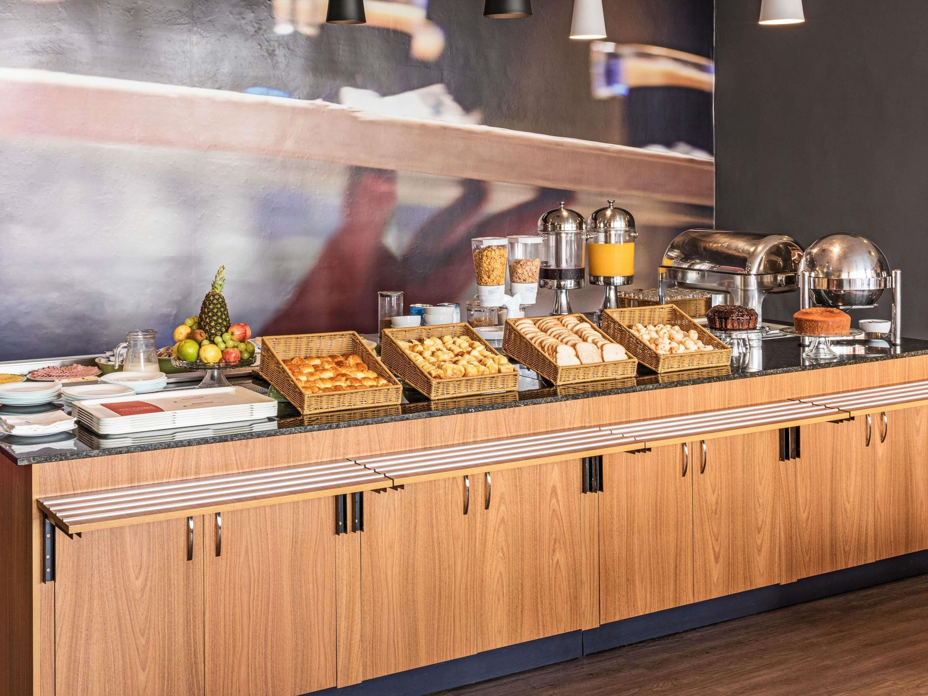A buffet counter with various food items and beverages, including bread, pastries, and fruits.