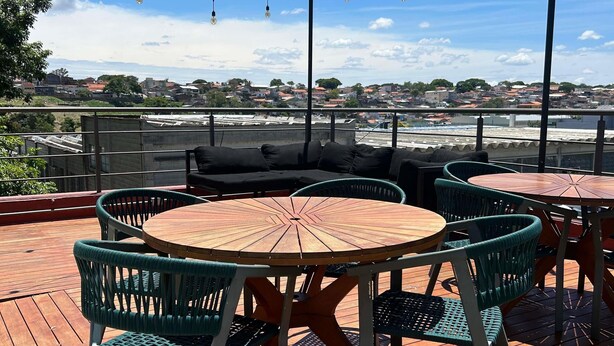 A rooftop terrace with round wooden tables and green wicker chairs, overlooking a residential area. - ibis Sao Jose dos Campos Dutra (São José dos Campos)