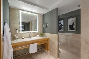 Un baño moderno con un espejo grande, un tocador de madera, un perchero, una planta y obras de arte enmarcadas en la pared.