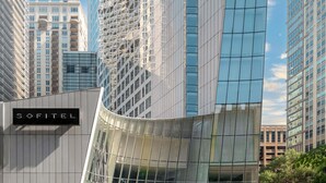 Un immeuble moderne de grande hauteur, doté d’une façade incurvée en verre, entouré d’autres bâtiments imposants.