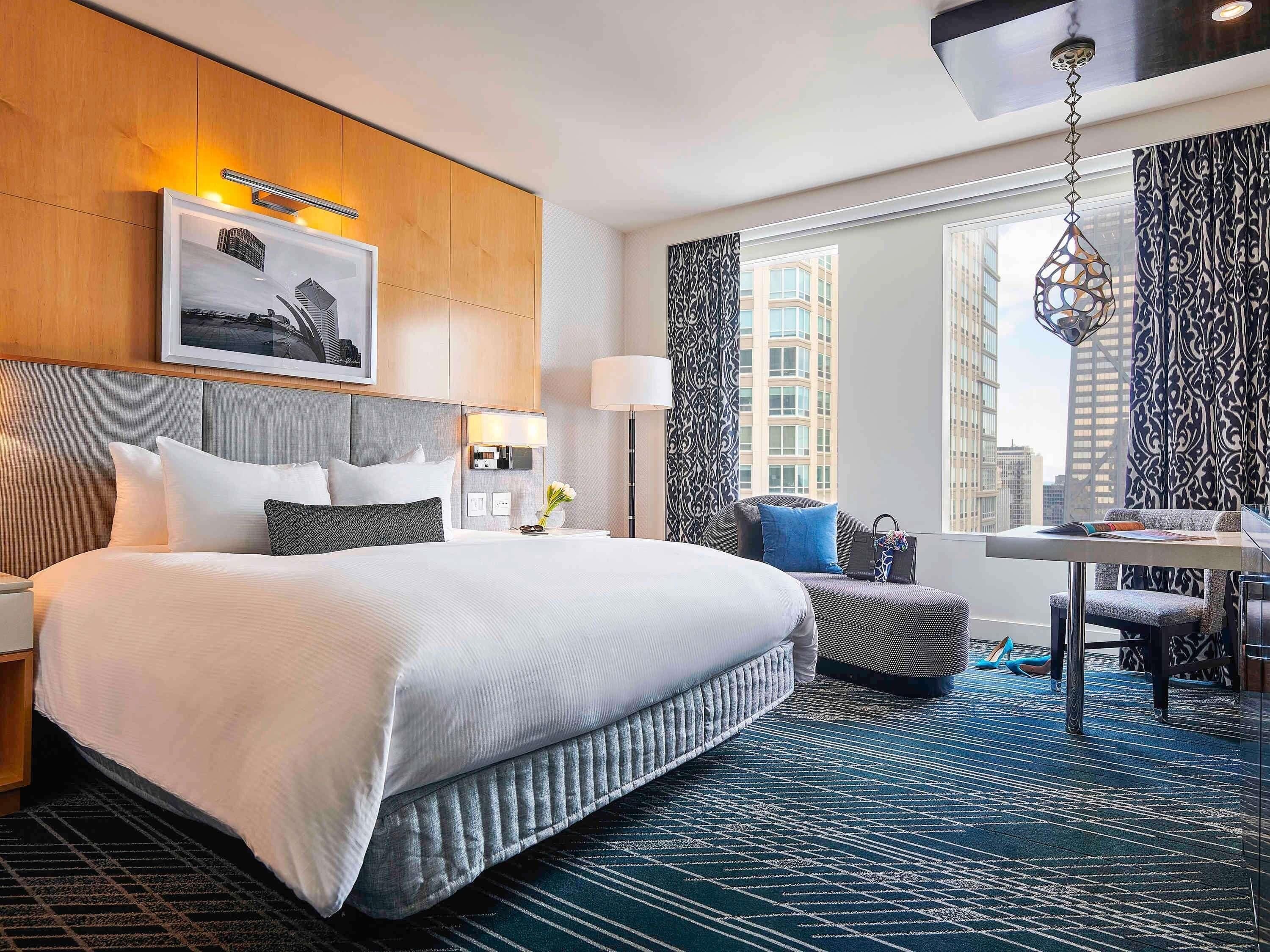 Quarto de hotel com uma cama grande, uma mesa de trabalho e vista para a cidade.