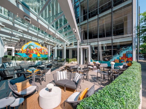 An outdoor seating area with tables and chairs, a mural, and a glass atrium.