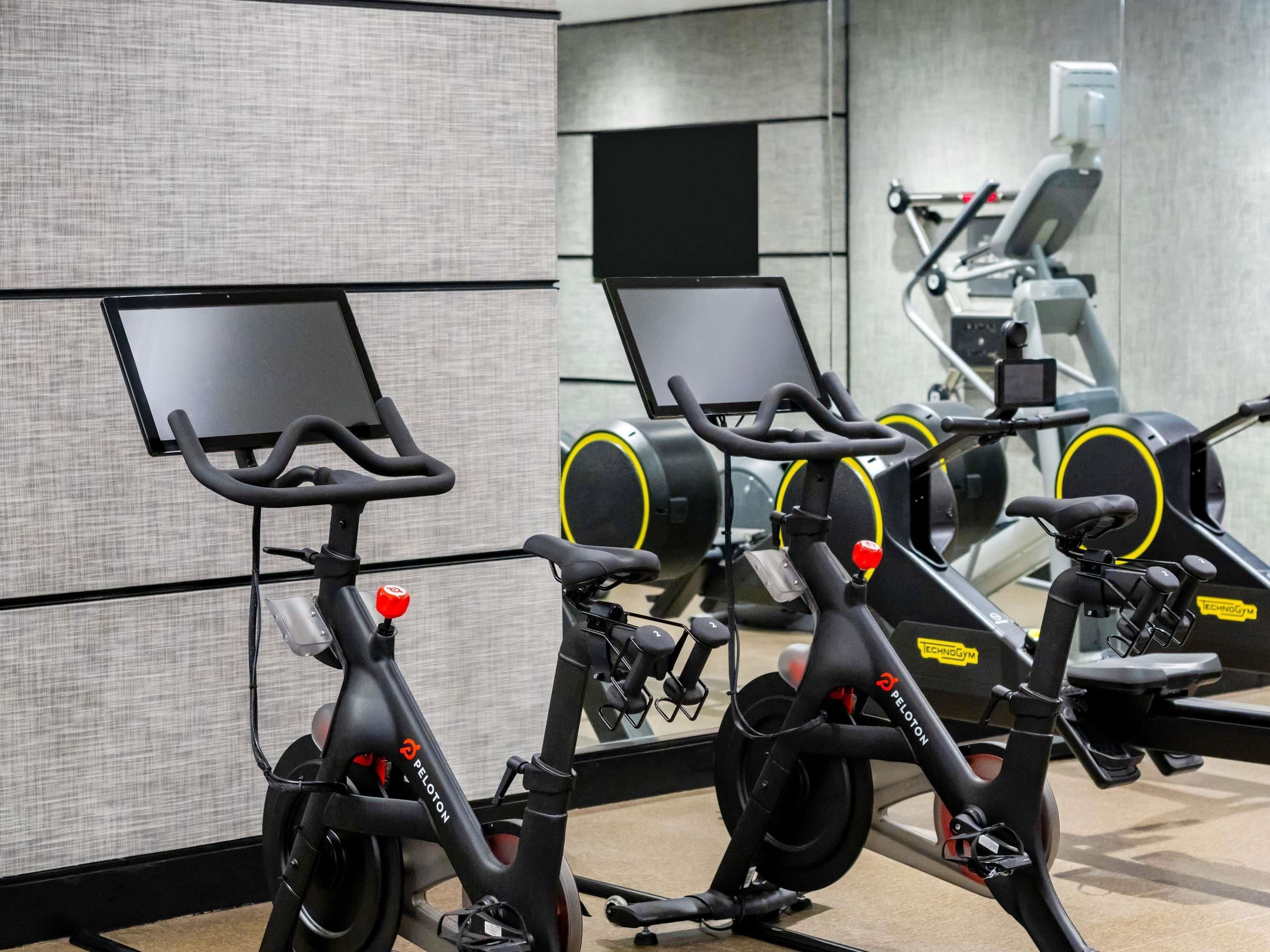 Stationary bikes with attached screens, arranged in a gym setting.