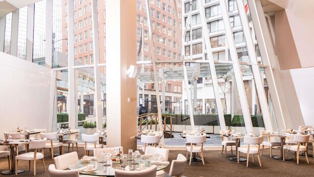 Un espace de restauration moderne avec des tables et des chaises rondes, de grandes fenêtres et une vue sur le paysage urbain.