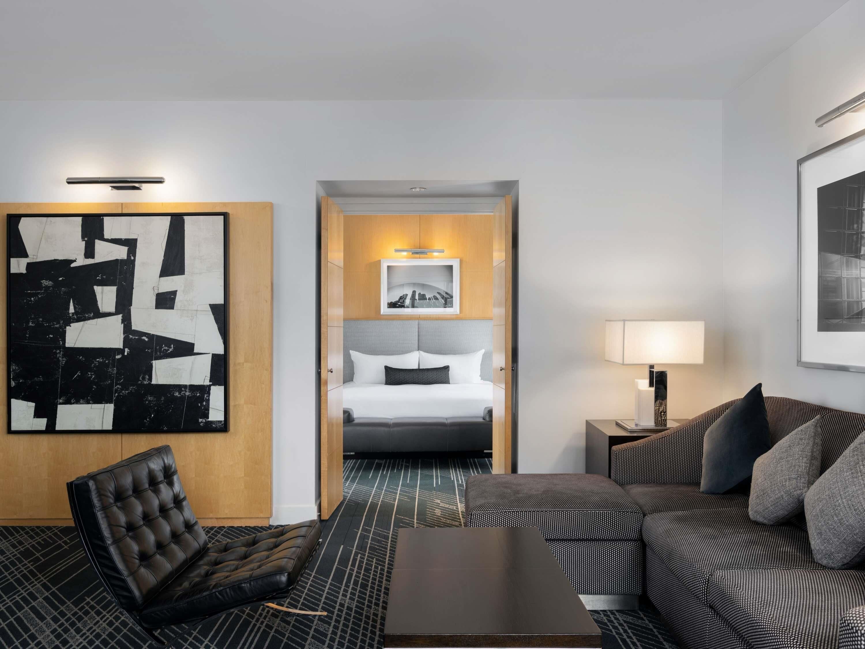 Une chambre d’hôtel comprenant un lit, un canapé, une chaise, une table basse et un grand tableau abstrait.