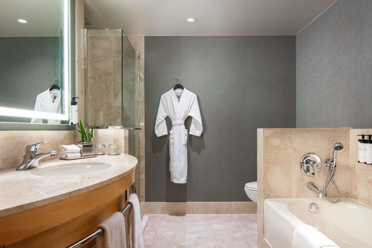 A modern bathroom with a marble vanity, a glass shower enclosure, a white robe hanging on the wall, and a separate bathtub area.