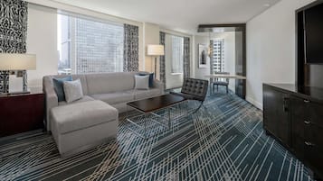 A modern hotel room with a sofa, ottoman, coffee table, and a TV.