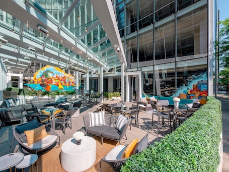 An outdoor seating area with tables and chairs, a mural, and a glass atrium.. Sofitel Chicago Magnificent Mile